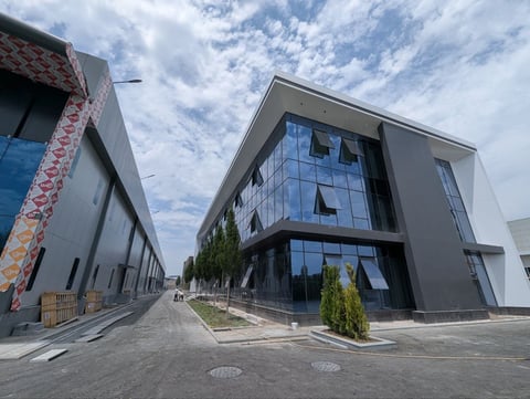 Modern industrial buildings with glass facades and gray concrete walls along a paved street under cloudy sky