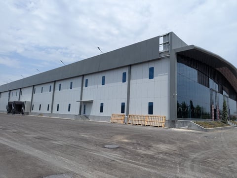 Modern industrial warehouse building with white corrugated metal siding and dark roof under partly cloudy sky