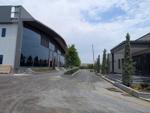 Modern curved building with glass facade beside driveway and landscaping on sunny day