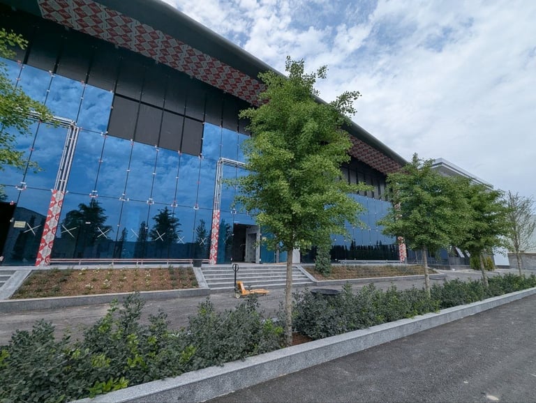Modern building exterior with large blue glass windows, climbing ivy, brick accents, and manicured landscaping under cloudy sky