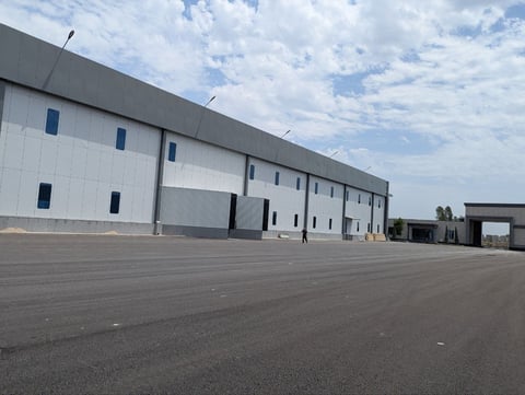 Large modern warehouse or industrial building with white corrugated metal walls and loading docks on an empty asphalt parking lot