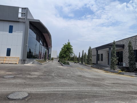 Modern courtyard with contemporary gray and stone buildings separated by green trees and landscaping under partly cloudy sky
