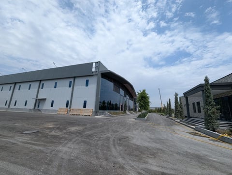 Modern industrial building with curved architecture and concrete driveway under blue cloudy sky